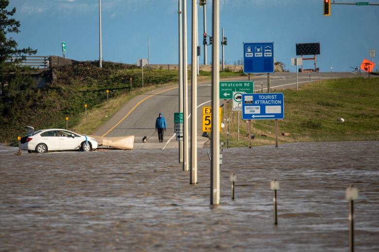 A road is submerged under floodwaters, with signs indicating tourist attractions and other roads around the corner.