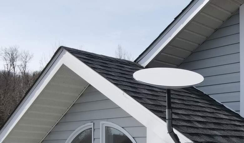 A flat satellite dish attach to the roof of a house.