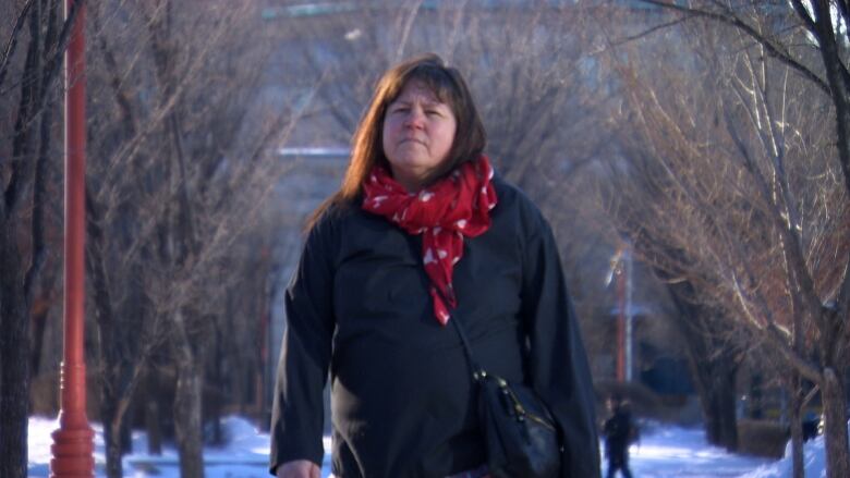 A woman wearing a black parka and red scarf poses for a photo. 