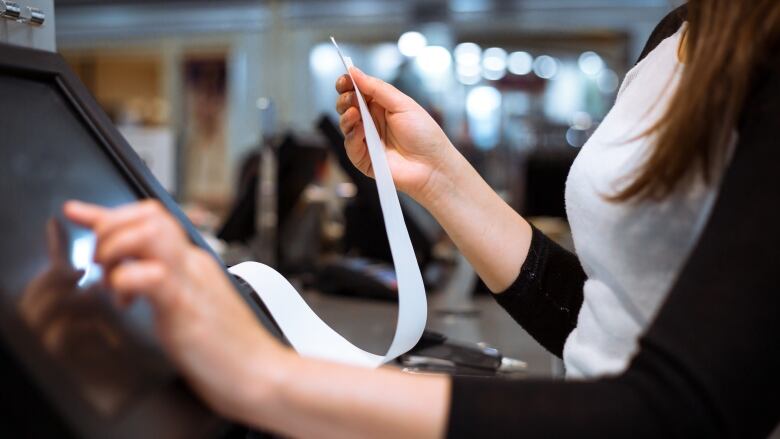 A woman looks at a receipt at a cash register.