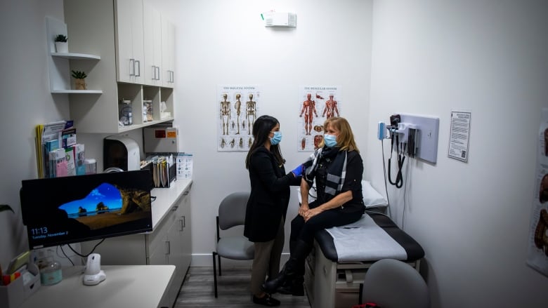 A nurse practitioner takes the blood pressure of a patient in a clinic room.