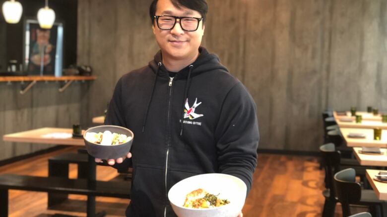 A man holds up two bowls of food in a restaurant.