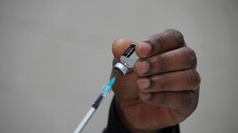 A close-up of a hand holding a vaccine vial as a needle is filled from it.