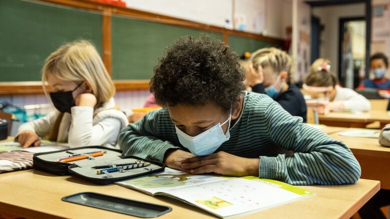 Elementary school students work at their desks while wearing medical masks. 