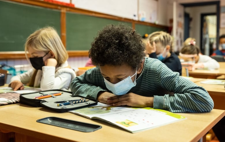 Elementary school students work at their desks while wearing medical masks. 