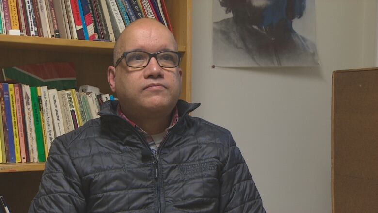 A man wearing a puffer jacket sitting in front of a book shelf