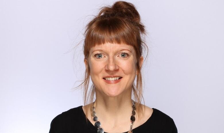 A smiling woman with short bangs and the rest of her hair tied up.