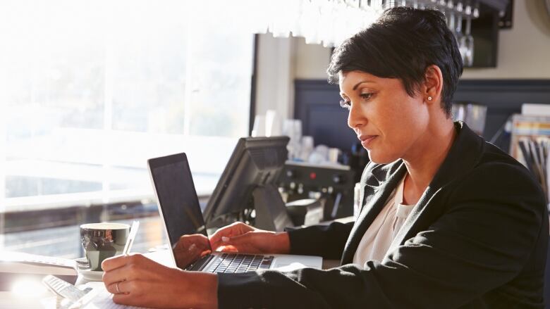 A woman with short dark hair in business casual attire sitting at a desk in front of a laptop.