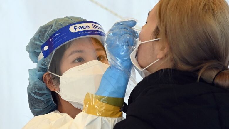 A health-care worker wearing full protective gear takes a nasal swab from a person whose medical mask is pulled down.