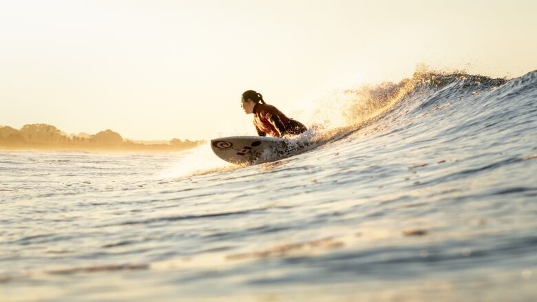 A woman low on her surfboard rides a small ocean wave.