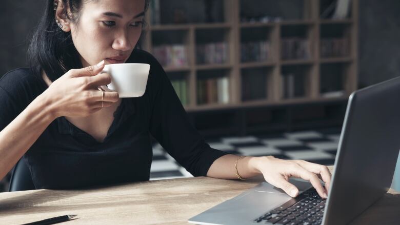 A woman sitting at  home desk drinking a coffee from a cup