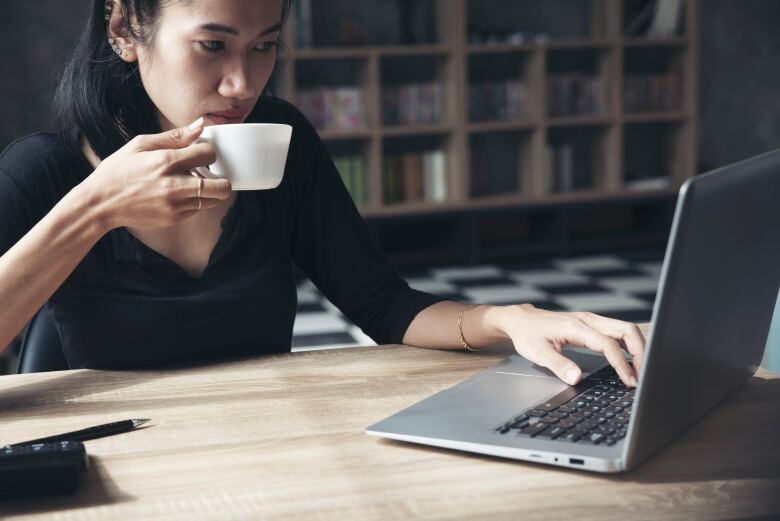 A woman sitting at  home desk drinking a coffee from a cup