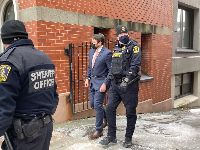 Man in suit led by officer in handcuffs