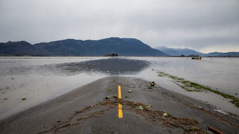 A photo taken from the middle of a highway shows the road disappearing under floodwaters. Mountains can be seen in the distance.