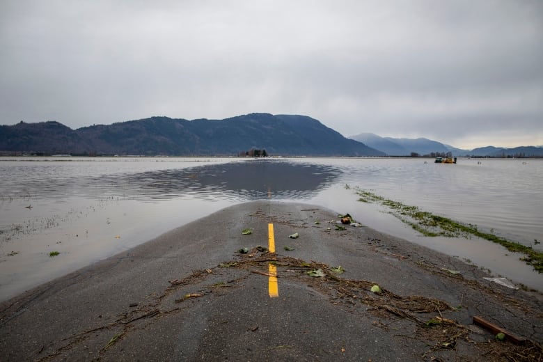 A photo taken from the middle of a highway shows the road disappearing under floodwaters. Mountains can be seen in the distance.