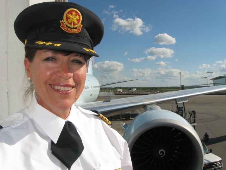 A woman wearing a pilot's outfit smiles in front of a plane.