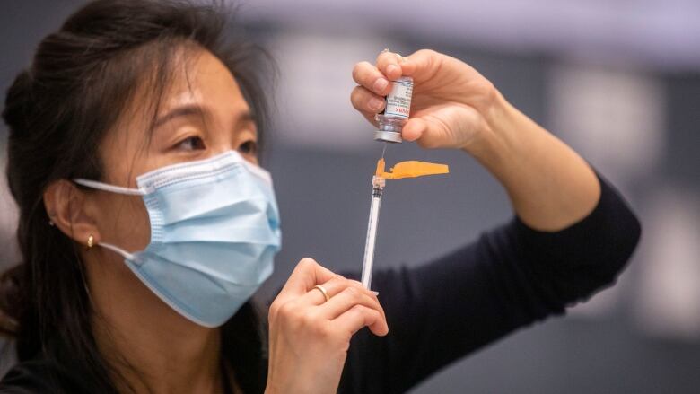 An East Asian woman wearing a mask loads a needle with COVID-19 vaccine.