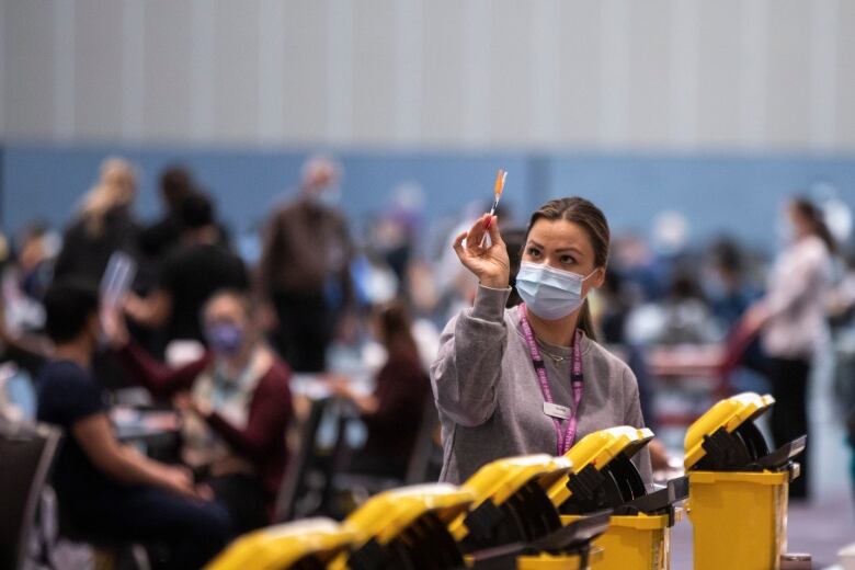 A female medical worker wearing a mask holds up a dose of COVID-19 vaccine at a Vancouver immunization clinic in January 2022. 