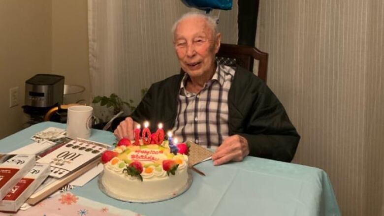 An older Japanese man smiles as he sits in front of a cake with '100' candle on it.