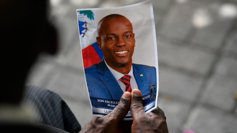 A person's hands hold a photo of Jovenel Moise, the former president of Haiti.