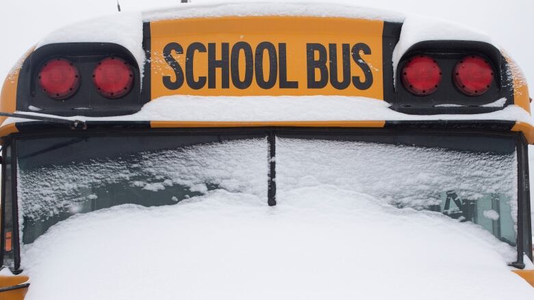 A close-up of the front of a school bus, showing a snow-covered windshield. The words, School Bus, can be seen at the top of the vehicle.