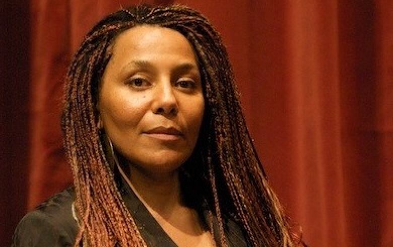 A Black woman with red, long braids poses in front of a red curtain.