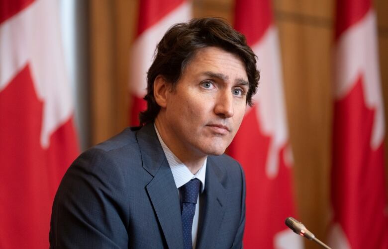 A man looks off camera, with Canadian flags in the background.