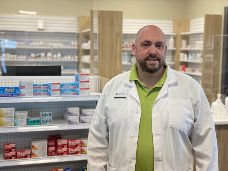 A portrait of a man wearing a white lab coat in a pharmacy.