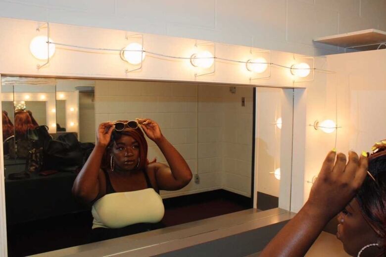 A Black woman adjusts her sunglasses on the top of her head in a mirror