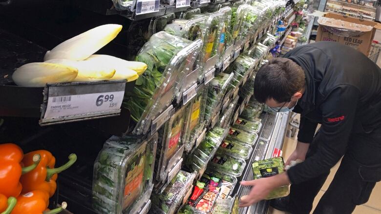 A man looks at packages of salad greens in a grocery store produce section. 