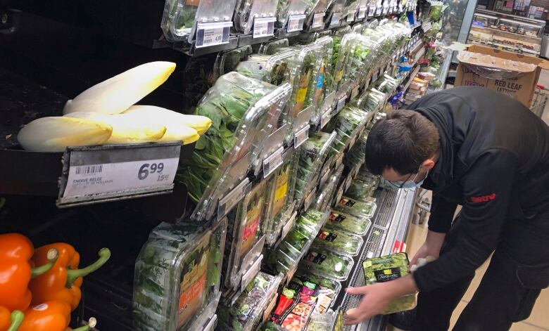 A man looks at packages of salad greens in a grocery store produce section. 