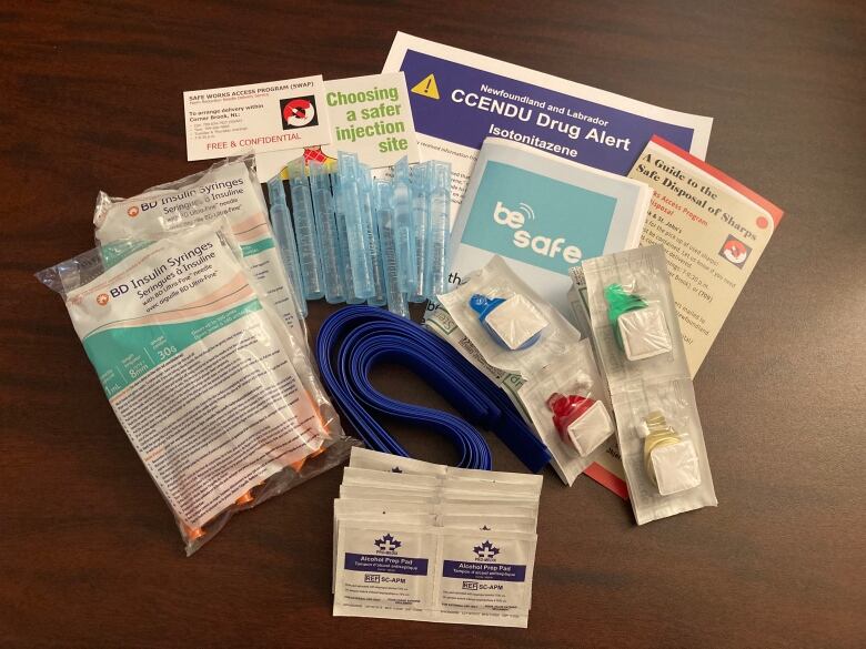 Needles, cookers, wipes, containers and pamphlets are spread out on a table. 