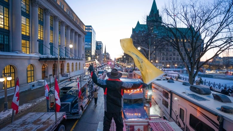 Someone in a cowboy hat waves a yellow flag over rows of trucks parked on a city street.