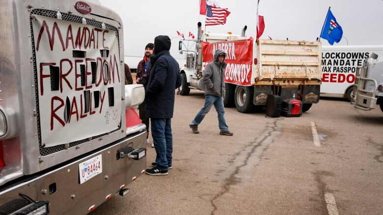 Convoy protesters walk among trucks emblazoned with protest signs.