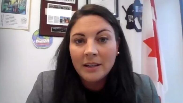 A woman with long dark hair in an office with plaques on the wall behind her.