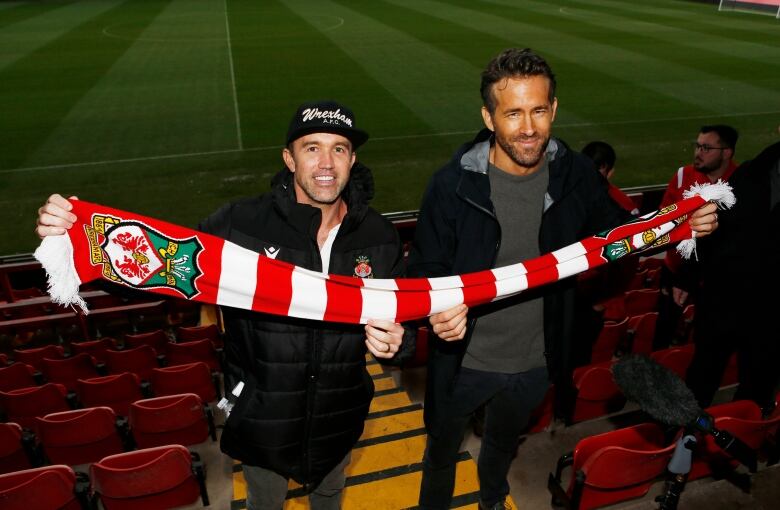 Two men hold a soccer team's branded scarf.