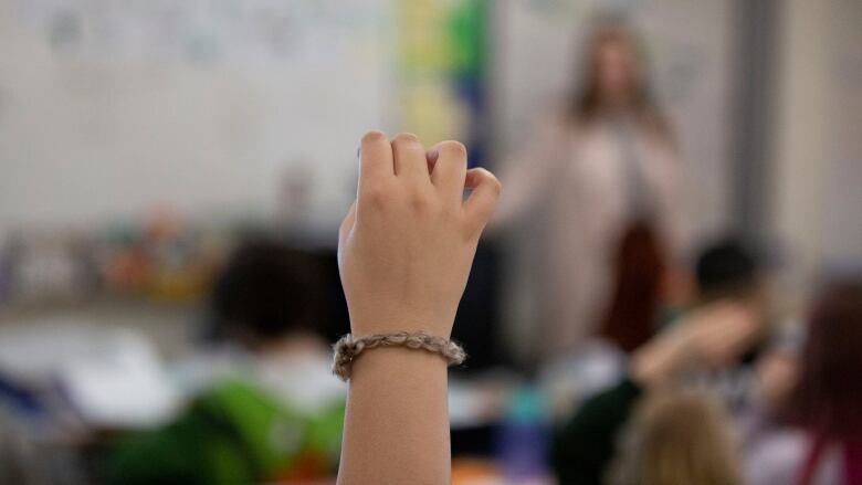 A child's hand is seen raised in a classroom.