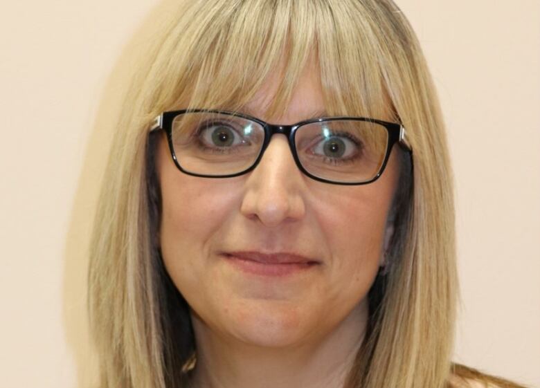 A blonde woman with black glasses poses for a headshot.