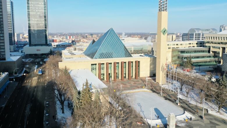 An aerial view of Edmonton city hall in the winter: a building with a glass triangle on top, and a snowy plaza in front.