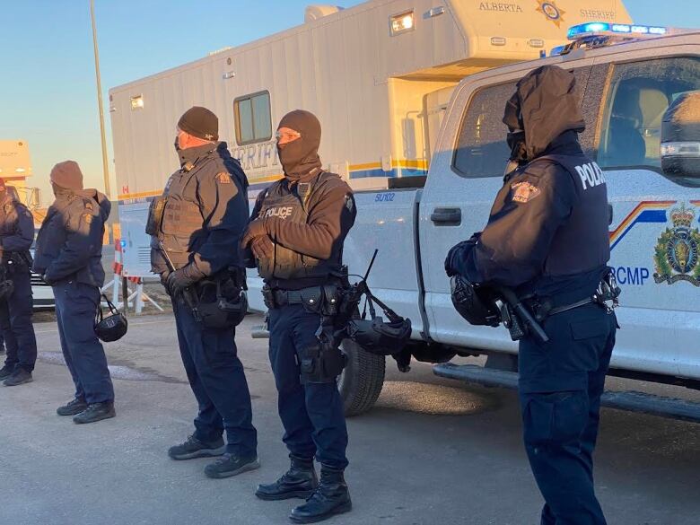 Four RCMP officers stand in front of RCMP vehicles.