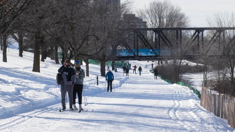 People cross-country ski on a groomed path next to a river.