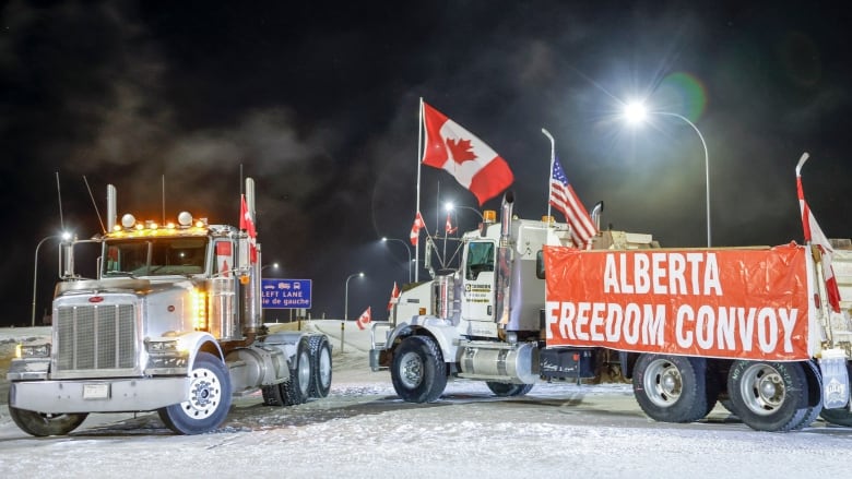 Two trucks blocking a highway at night.