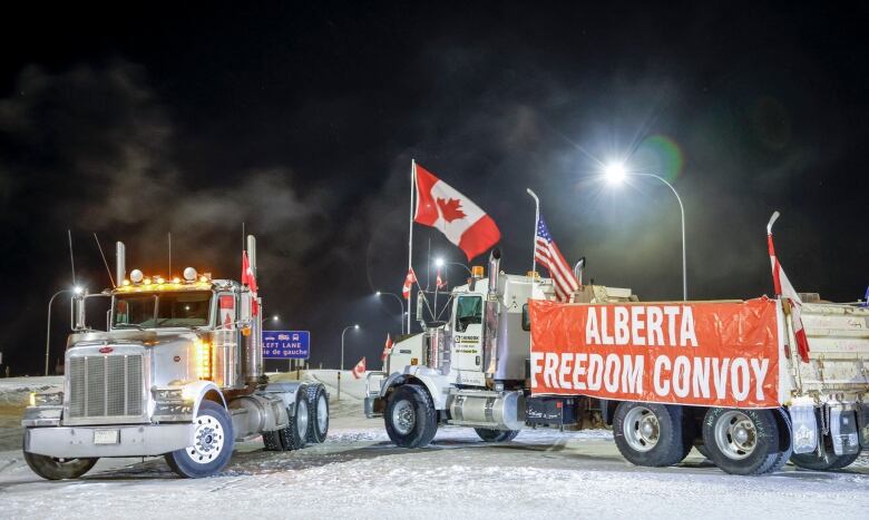 Two trucks blocking a highway at night.