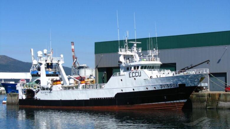 A large white ship is docked next to a green and grey building.