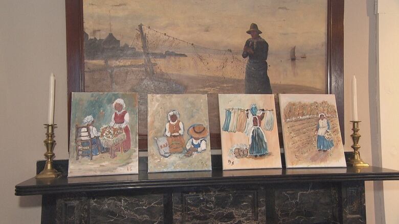 Five paintings on a fireplace mantle. They show a woman cooking, cleaning, hanging laundry, sowing seeds in a field and a man on a beach