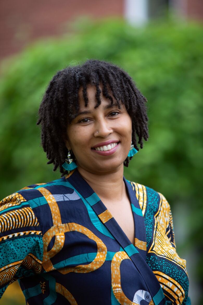 A Black woman with locs wearing a colourful blouse