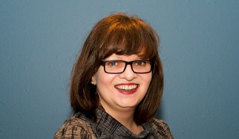 A white woman with brown hair wearing glasses and a brown top