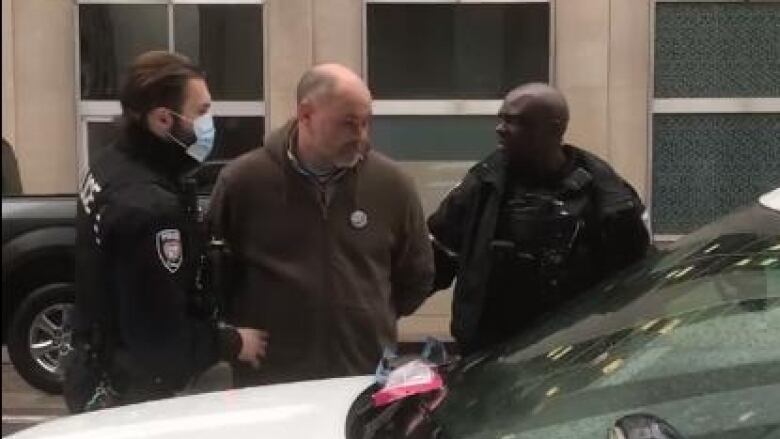 A man led toward a police vehicle by two officers.