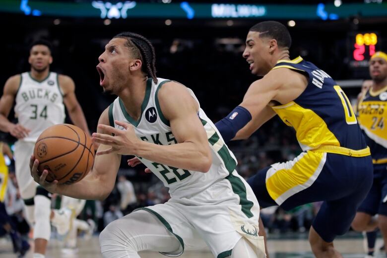 Two players on a basketball court. One is wearing Milwaukee Bucks jersey and has the ball. The other is a Pacers player