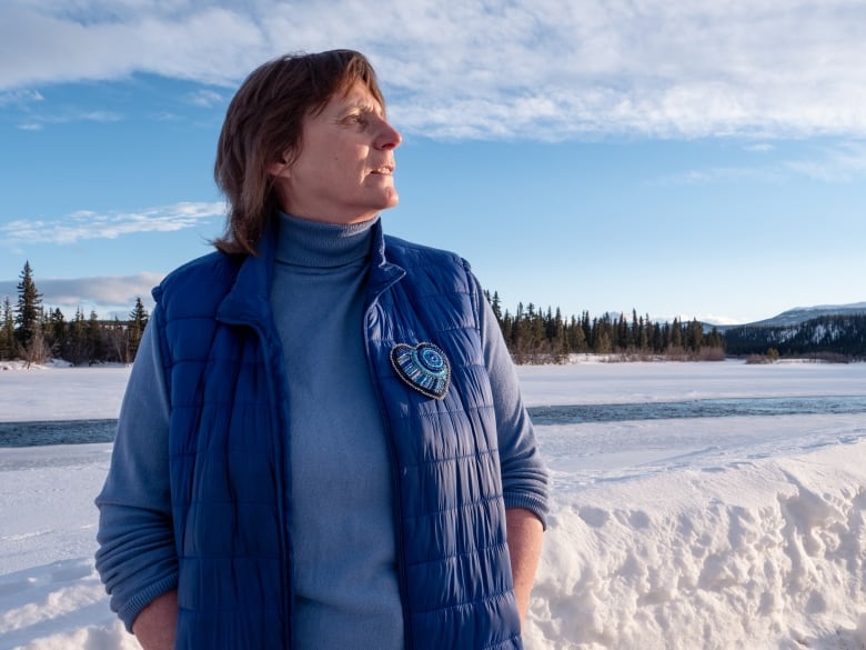 A woman stands beside a frozen river.